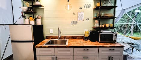 Una cucina compatta con lavello, mobili, forno a microonde e lampada a sospensione.