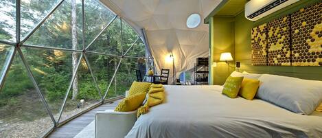 Een moderne tentkamer met een groot bed, een zithoek en uitzicht op het bos.