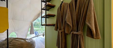 A tented room with a bed, a rack of towels, and a view of the outdoors.