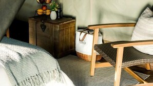 A tented room with a bed, a chair, a small wooden chest, and a window with a view of trees.
