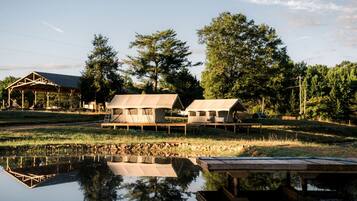 A rustic cabin with a wooden deck, a small dock, and a reflection in the water.