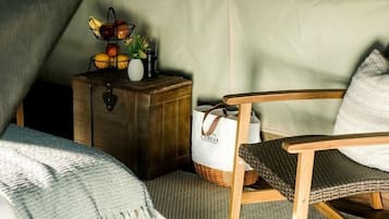 A tented room with a bed, a chair, a small wooden chest, and a window with a view of trees.