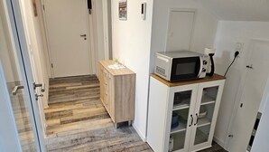 Un couloir avec un plancher en bois, une armoire avec des tiroirs, un four à micro-ondes posé sur le dessus, et une porte avec une serrure.