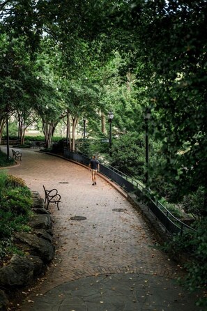 A curved brick pathway in a park with benches and a metal railing.