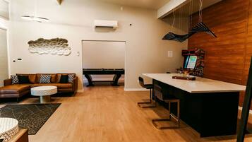A modern living room with a sofa, a pool table, and a bar area with stools.