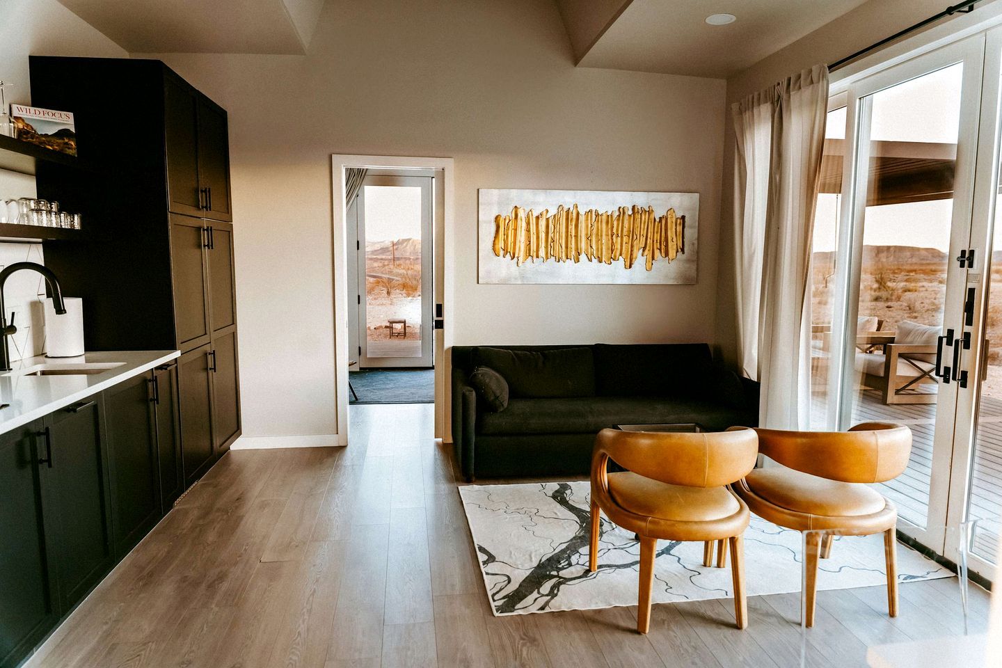 A modern interior with a kitchen, a dark green sofa, two leather chairs, and a large abstract painting.