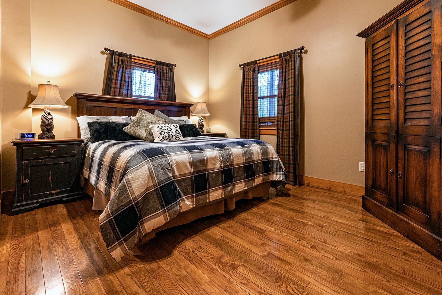 Un dormitorio con una cama de madera, dos mesitas de noche con lámparas, un armario de madera y ropa de cama a cuadros.