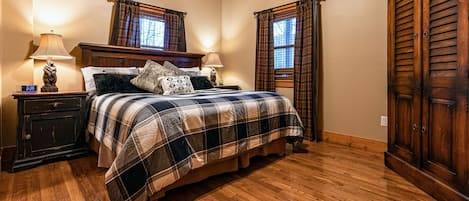 Un dormitorio con una cama de madera, dos mesitas de noche con lámparas, un armario de madera y ropa de cama a cuadros.