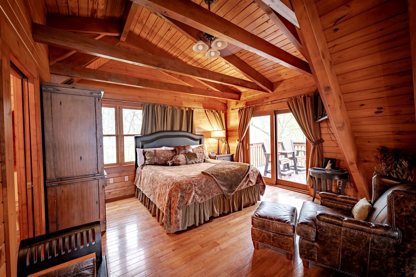 Ein Schlafzimmer in einer Blockhütte mit einem großen Bett, Holzwänden, einem Deckenventilator und Blick ins Freie.