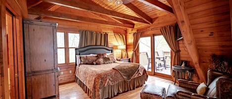 Ein Schlafzimmer in einer Blockhütte mit einem großen Bett, Holzwänden, einem Deckenventilator und Blick ins Freie.