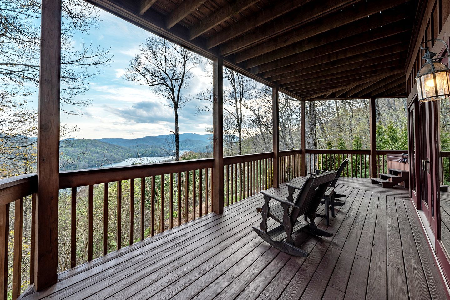 A wooden deck with a view of a lake and mountains, a rocking chair, and a bench.