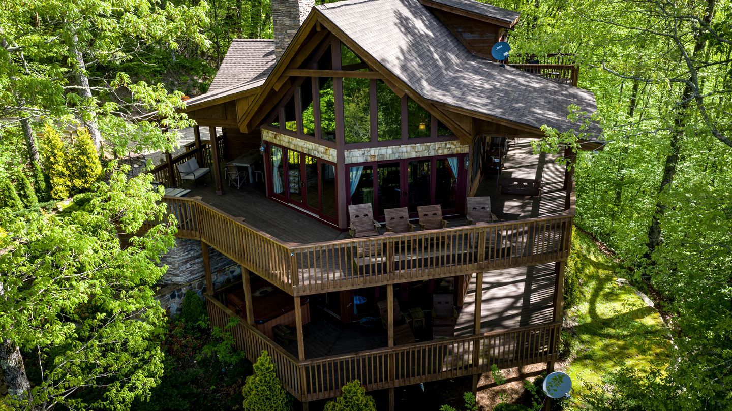 A multi-level wooden cabin with balconies, surrounded by dense forest.