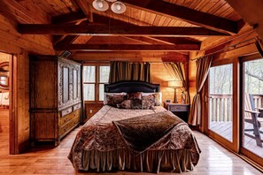 Ein Schlafzimmer einer Holzhütte mit einem Bett, einem Nachttisch, einer Kommode und einem Fenster mit Blick auf eine Terrasse.