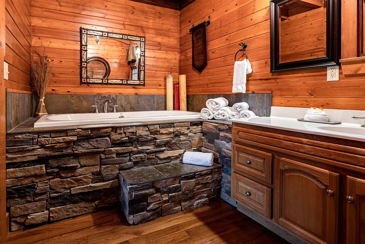 A bathroom with a stone accent wall, wooden cabinets, a large mirror, and a towel rack.
