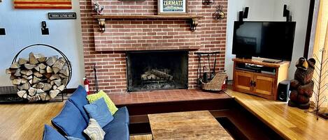 A living room with a brick fireplace, a television, and a sofa with blue cushions.