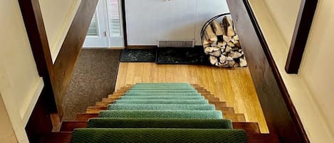Una escalera de madera con alfombra verde, un cuadro en la pared y una chimenea con leña.