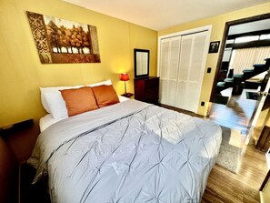 Habitación de hotel con cama, mesita de noche, lámpara, espejo, armario y vistas al exterior.