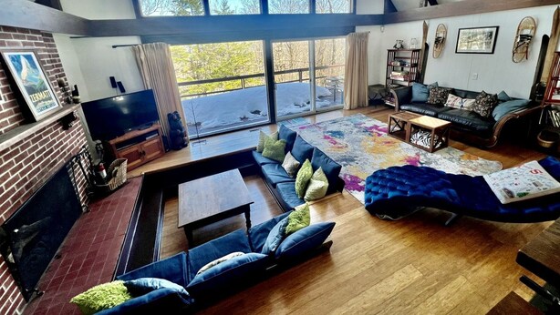A spacious living room with a large window, a fireplace, a sofa set, and a coffee table. - Unbelievable Cabin with Amazing Sights and Fire Pit in Winhall, Vermont (Winhall)