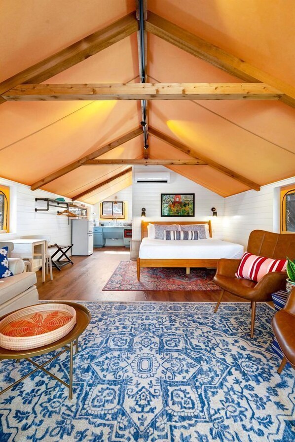 Une chambre confortable située dans les combles, avec un lit, une chaise, une petite table et un coin cuisine à l’arrière-plan.