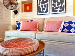 A sofa with patterned cushions, a woven basket, and a wall-mounted fan.