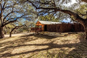 A rustic cabin with a wooden deck, surrounded by trees.