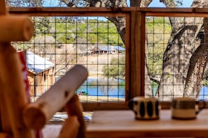 Vista a través de una ventana con marco de madera, una mesa con dos tazas y un vistazo a un muelle con un barco.