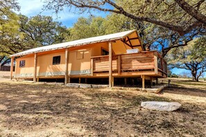 A single-story wooden cabin with a covered porch, a small deck, and a stone foundation.