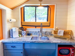 A compact kitchen with a sink, a coffee maker, a microwave, and a window with a view of trees.