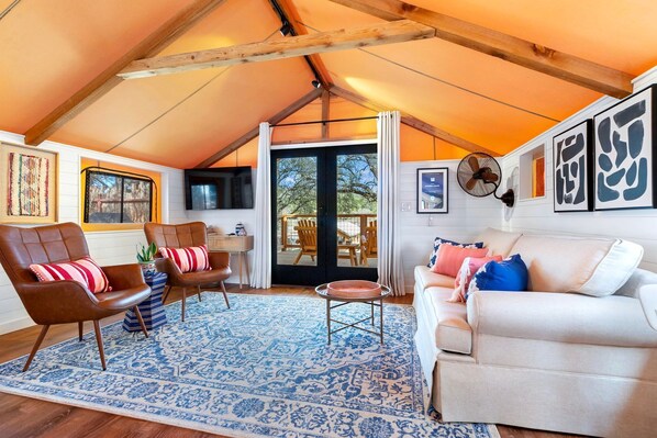 A cozy interior with a high ceiling, a sofa, a chair, a small table, and a fan.