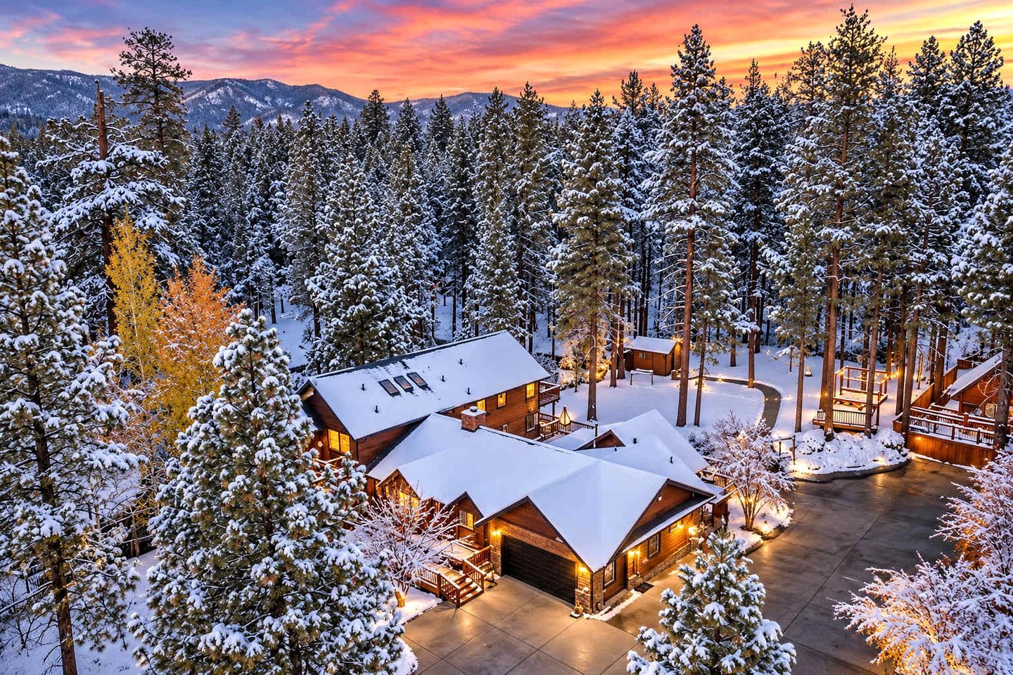 A lodge with multiple cabins surrounded by snow-covered trees, set against a mountainous backdrop.