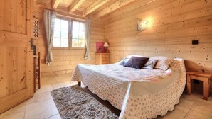 A wooden cabin bedroom with a bed, a nightstand, a window with curtains, and a wooden ceiling. - Luxury mountain chalet for 8 people Saint Gervais close to amenities (Saint-Gervais-les-Bains)
