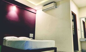 A hotel room with a bed, an air conditioning unit, a wall-mounted light, and a door leading to another room. - HOTEL KABAB JUNCTION (Bengaluru)