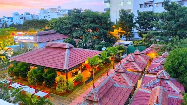 A traditional-style building with a red roof, surrounded by lush greenery and adjacent to a modern building labeled "GMR Nagar Junction". - HOTEL KABAB JUNCTION (Bengaluru)