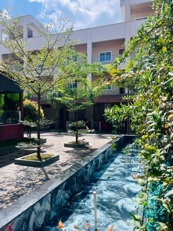 Un patio con un estanque de carpas, árboles en macetas y un edificio con balcones.