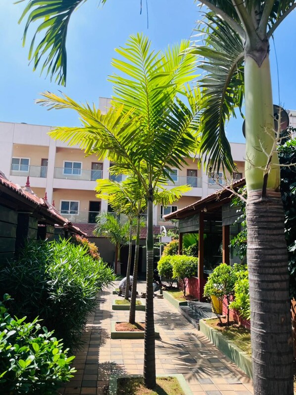 A courtyard with palm trees, a tiled pathway, and a building with a tiled roof in the background. - HOTEL KABAB JUNCTION (Bengaluru)