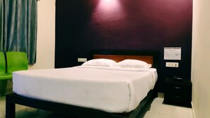 Ein ordentlich bezogenes Bett mit weißen Leinentüchern in einem Zimmer mit dunkler Wand und einem grünen Stuhl.