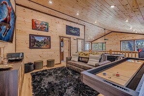 Interior de uma cabana de madeira com mesa de bilhar, sofá e obras de arte nas paredes.