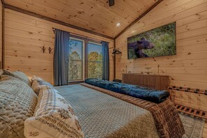 A wooden cabin bedroom with a bed, a window, a radiator, and a painting of a bear. - Charming Mountain Cabin with Hot Tub & Game Loft near Pigeon Forge, Tennessee (Sevierville)