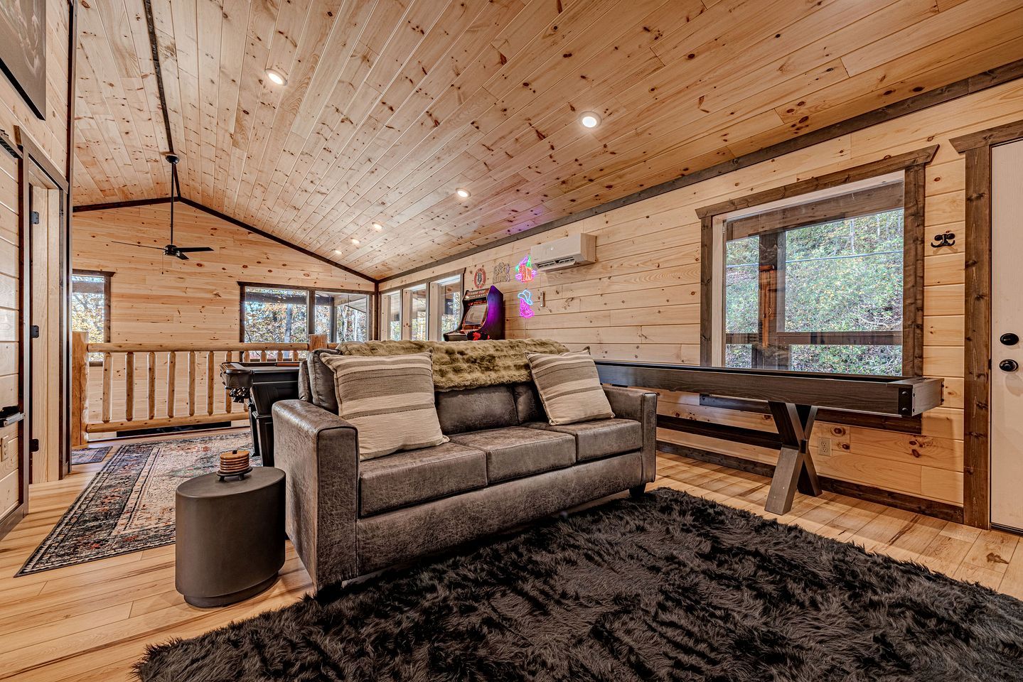 A cozy cabin interior with a wooden ceiling, a sofa, a small round table, and a large window.
