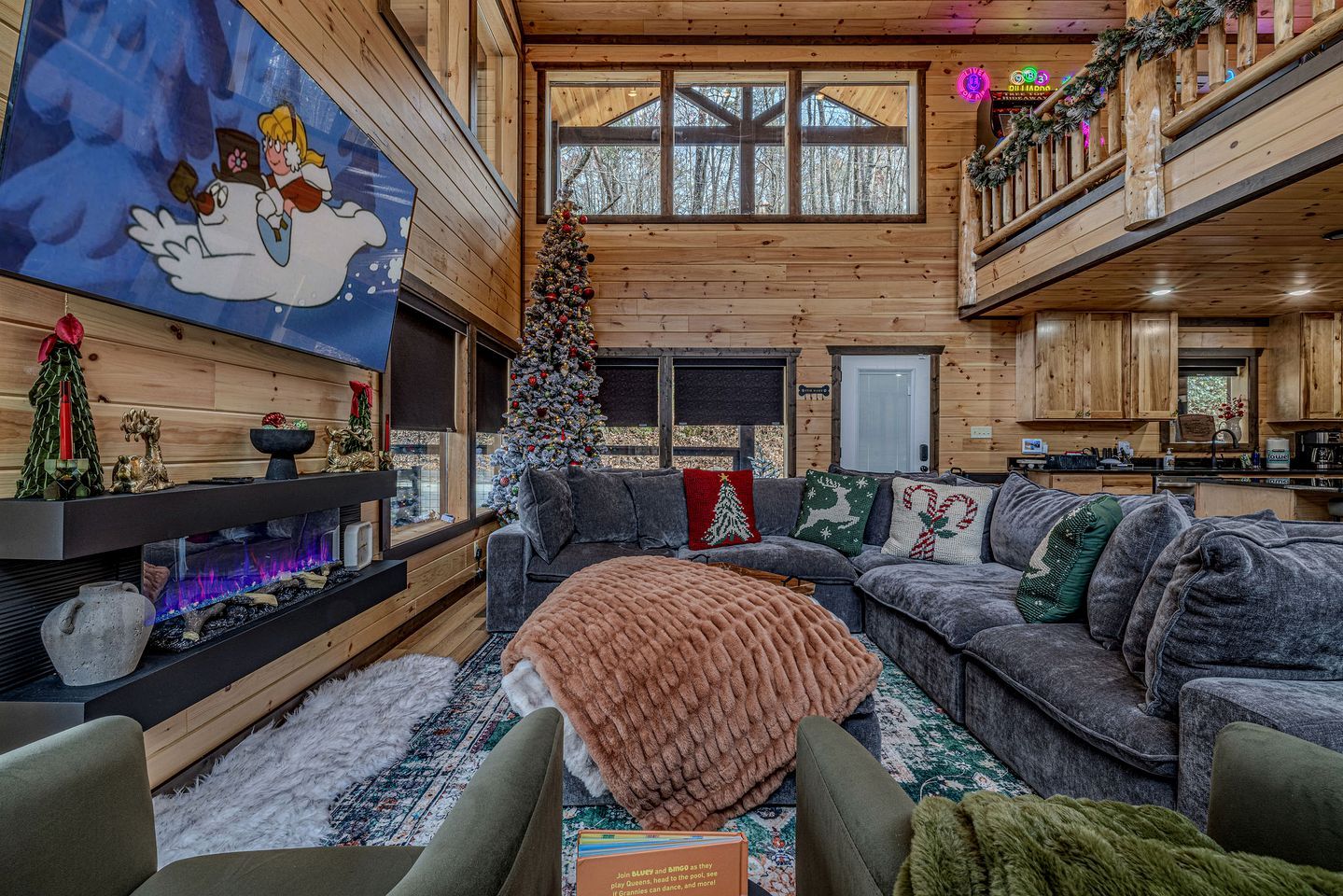 L’intérieur d’un chalet chaleureux, avec une cheminée, un sapin de Noël et un grand écran de télévision.