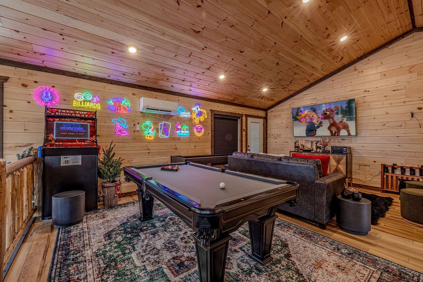 A pool table in a room with wooden walls, neon signs, and a large TV screen.