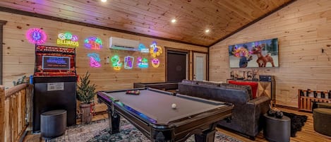A pool table in a room with wooden walls, neon signs, and a large TV screen.