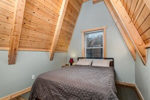 A bedroom with a sloped ceiling, a window, a bed, and a nightstand. - Fully-Equipped A-Frame with Beautiful Lake Views in Michigan (Au Gres)