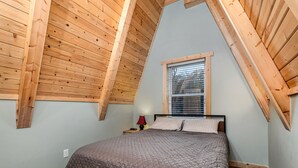 A bedroom with a sloped ceiling, a window, a bed, and a nightstand.