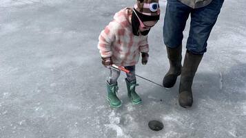 Un niño con un conjunto rosa y marrón está de pie sobre hielo, con un hombre cerca.