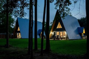 A modern, triangular-shaped building with a glass facade and a picnic table outside. - Fully-Equipped A-Frame with Beautiful Lake Views in Michigan (Au Gres)