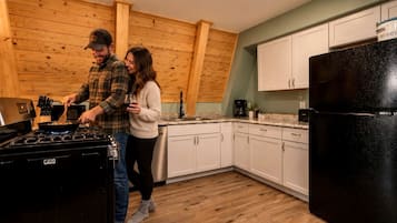 Una cocina con paredes de madera, armarios blancos, un refrigerador negro y una estufa a gas.