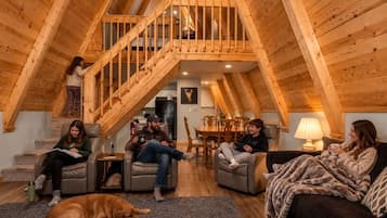 A cozy room with a wooden staircase, a dog, and four people sitting on sofas.