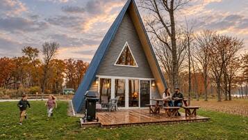 Una casa de forma triangular con una terraza, una parrilla y una mesa con sillas.