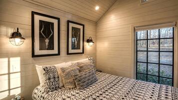 A bedroom with a bed, two wall-mounted lamps, and a window with a view of trees and a red building.